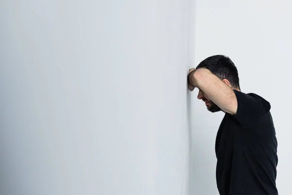 Adulte bouleversé homme en t-shirt noir debout par mur blanc — Photo de stock