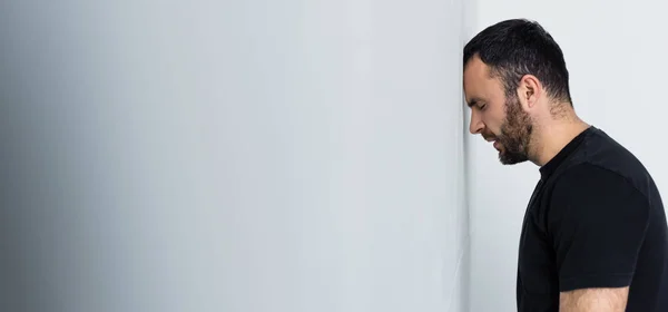 Панорамный снимок депрессивного бородатого мужчины, стоящего у белой стены с закрытыми глазами — стоковое фото