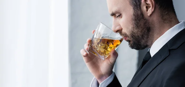 Panoramic shot of sad, handsome bearded man drinking whiskey — Stock Photo