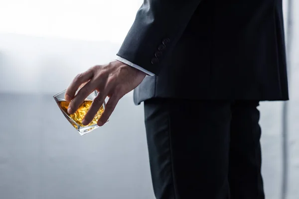 Teilbild eines Mannes im schwarzen Anzug mit einem Glas Whiskey — Stockfoto