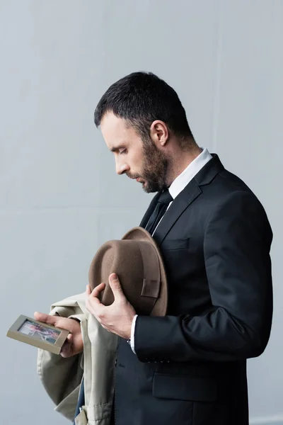 Hombre deprimido en traje mirando la foto en el marco mientras sostiene el sombrero en la mano - foto de stock