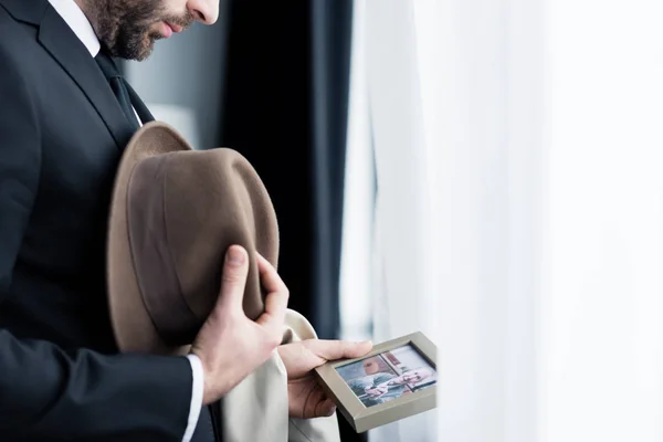 Partial view of man looking at photo in frame while holding hat in hand — Stock Photo