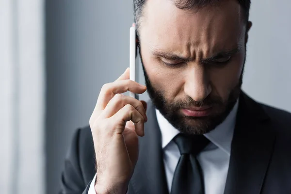 Hombre barbudo serio en traje negro mirando hacia abajo mientras se utiliza el teléfono inteligente - foto de stock