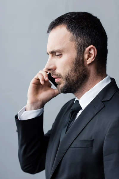 Hombre barbudo reflexivo, guapo en traje negro usando teléfono inteligente y mirando hacia abajo - foto de stock