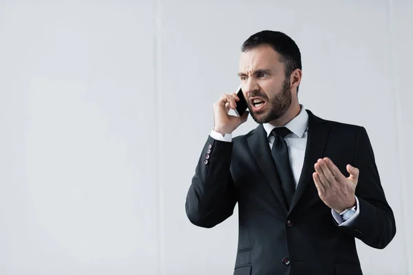 Hombre de negocios enojado en traje negro peleando mientras habla en el teléfono inteligente - foto de stock