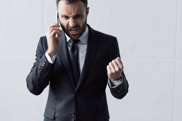 Hombre de negocios enojado en traje negro gritando mientras habla en el teléfono inteligente - foto de stock