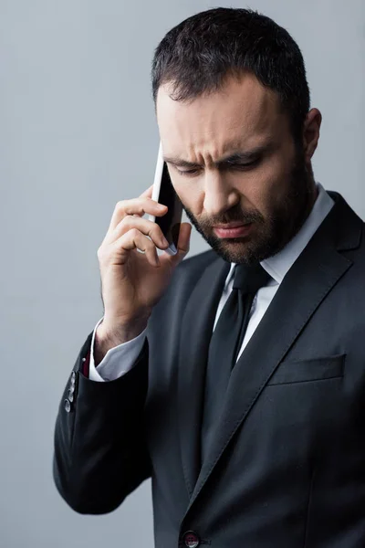 Hombre barbudo reflexivo en suite negro mirando hacia abajo mientras se utiliza el teléfono inteligente - foto de stock