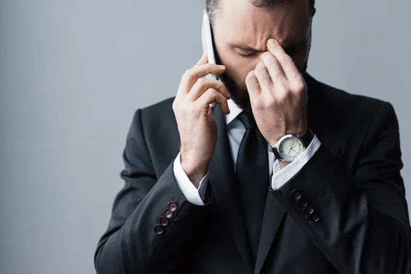 Hombre molesto en traje negro usando un teléfono inteligente con los ojos cerrados y sosteniendo la mano cerca de la cara - foto de stock