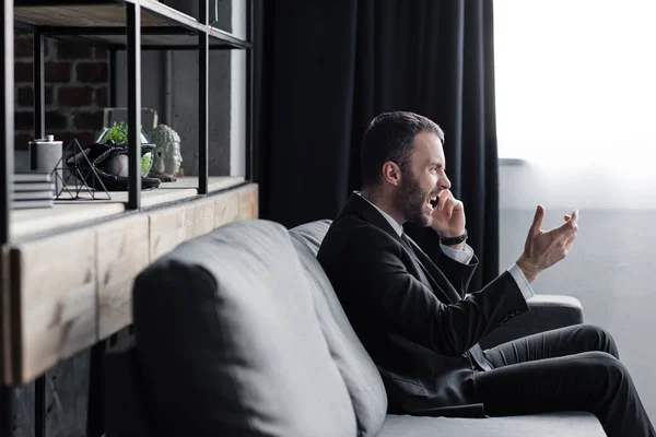 Сердитий чоловік сидить на дивані і сварки під час розмови на смартфоні в офісі — стокове фото