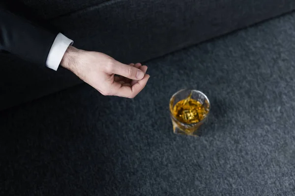 Vista parcial del hombre acostado en un sofá cerca de un vaso de whisky en el suelo - foto de stock