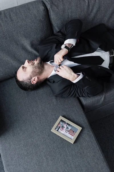 Vista aerea di uomo d'affari depresso sdraiato sul divano vicino alla foto in cornice — Foto stock