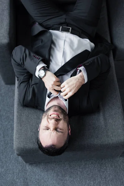 Вид сверху на подавленного бизнесмена, развязывающего галстук, лежащего на диване — стоковое фото