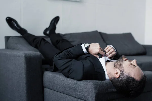 Selective focus of depressed businessman suffering while lying on sofa — Stock Photo