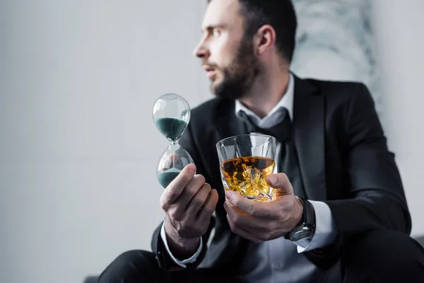 Selektiver Fokus frustrierter Geschäftsleute mit Glas Whiskey und Sanduhr — Stockfoto