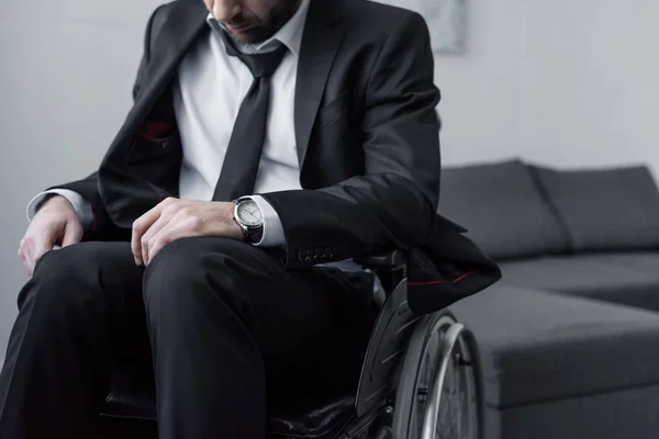 Cropped view of disabled man in black suit sitting in wheelchair with bowed head — Stock Photo