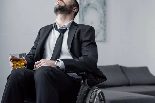 Vue recadrée de l'homme handicapé déprimé en costume assis en fauteuil roulant avec un verre de whisky — Photo de stock