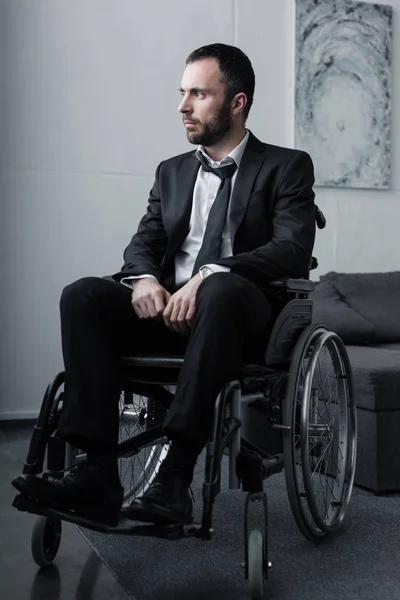 Homem deficiente pensivo em terno preto sentado em cadeira de rodas e olhando para longe — Fotografia de Stock