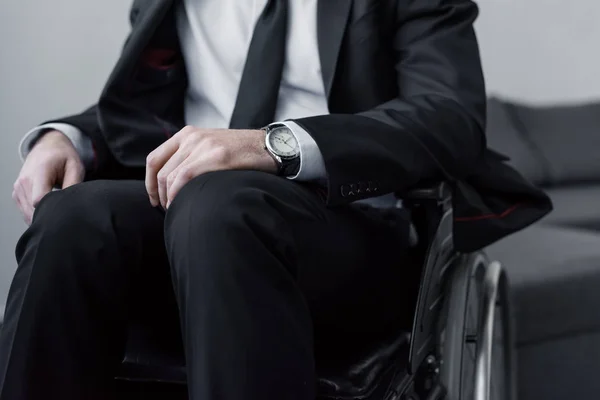Частичный вид инвалида в черном костюме и часы, сидящие в инвалидном кресле — стоковое фото