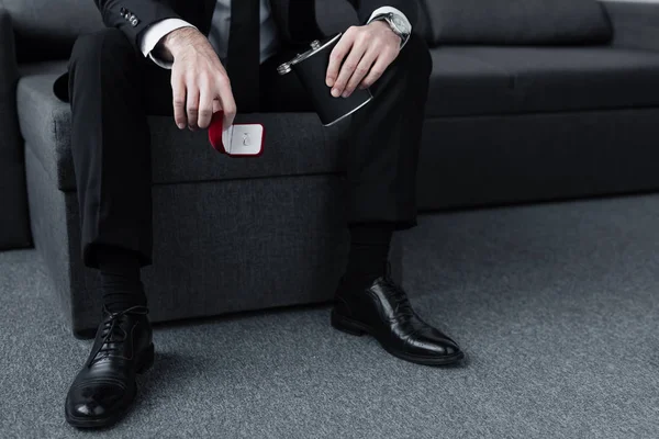 Cropped view of sitting man holding flask and gift box with ring — Stock Photo