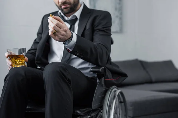 Vue recadrée de l'homme handicapé en costume assis en fauteuil roulant et tenant anneau et verre de whisky — Photo de stock
