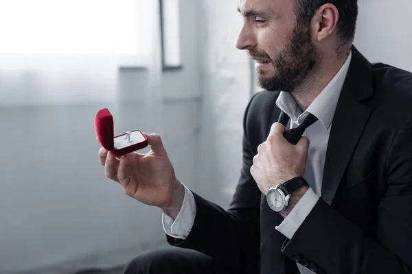 Depressed bearded man crying while looking at gift box with ring — Stock Photo