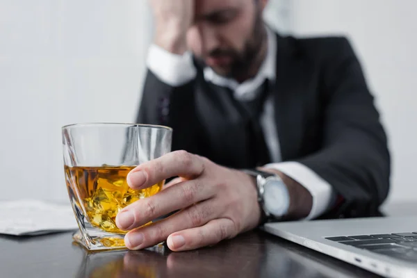 Selective focus of depressed businessman holding glass of whiskey — Stock Photo