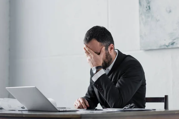 Расстроен бизнесмен, держась за лицо, сидя на рабочем месте — стоковое фото