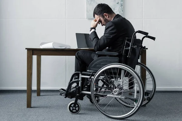 Deprimido empresário deficiente sentado em cadeira de rodas no local de trabalho com a cabeça curvada — Fotografia de Stock