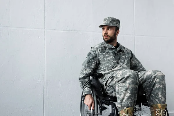 Pensive disabled military man in uniform sitting in wheelchair and looking away — Stock Photo