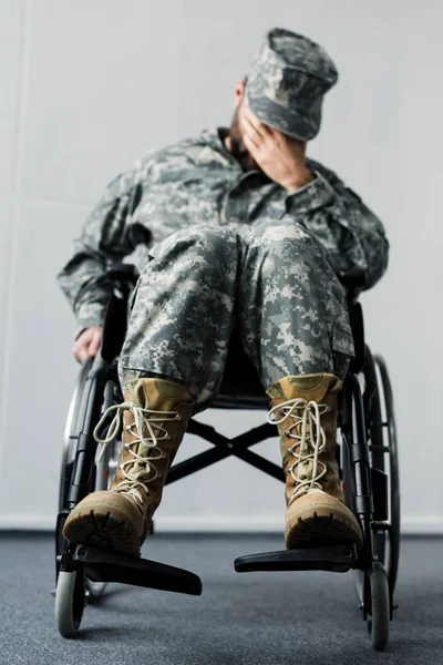 Messa a fuoco selettiva del militare disabile in uniforme seduto in sedia a rotelle e volto di copertura con mano — Foto stock