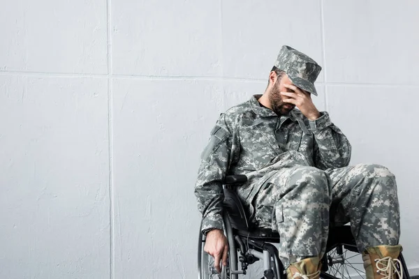 Depressed disabled military man in uniform sitting in wheelchair and holding hand on face — Stock Photo