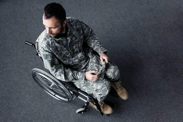 Vista aérea del hombre discapacitado en uniforme militar sentado en silla de ruedas y mirando hacia otro lado - foto de stock
