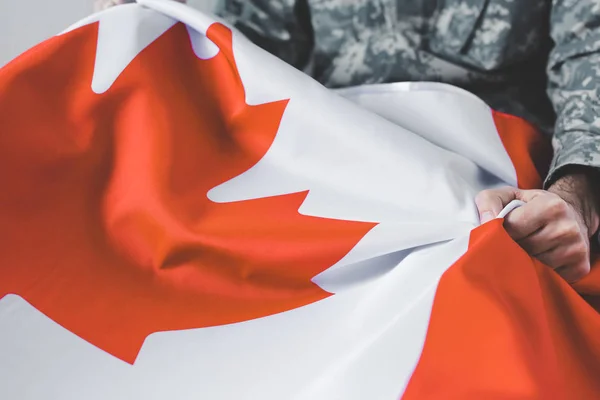Enfoque selectivo del hombre en uniforme militar que sostiene la bandera nacional de Canadá - foto de stock