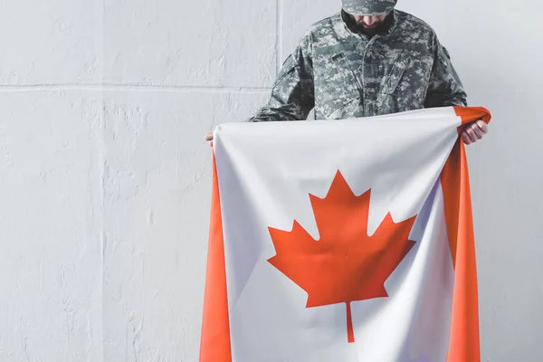 Homem de uniforme militar segurando bandeira nacional do Canadá enquanto estava perto da parede branca com cabeça curvada — Fotografia de Stock