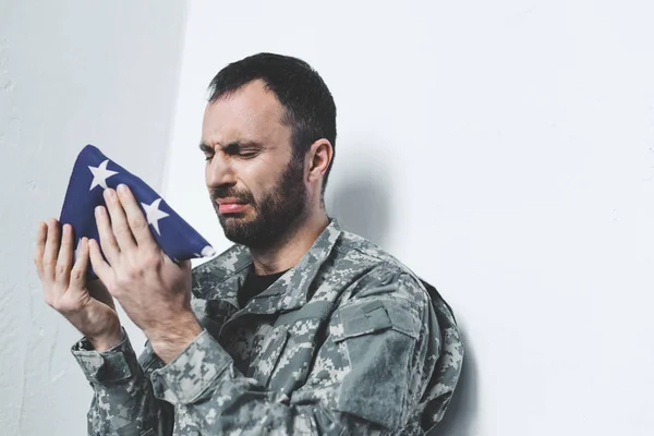 Depressed bearded military man crying while sitting by wall and holding usa national flag — Stock Photo
