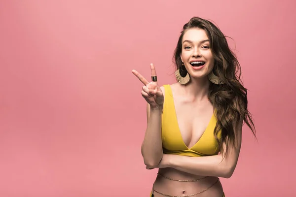 Lächelndes sexy Mädchen im gelben Badeanzug zeigt Friedenszeichen isoliert auf rosa — Stockfoto