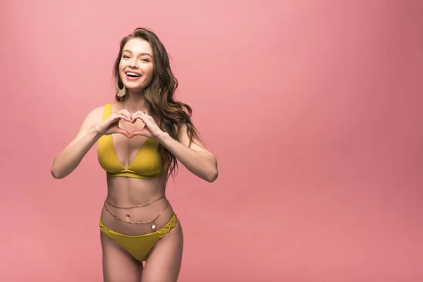 Lächelndes Mädchen im gelben Badeanzug mit Herzzeichen auf rosa — Stockfoto