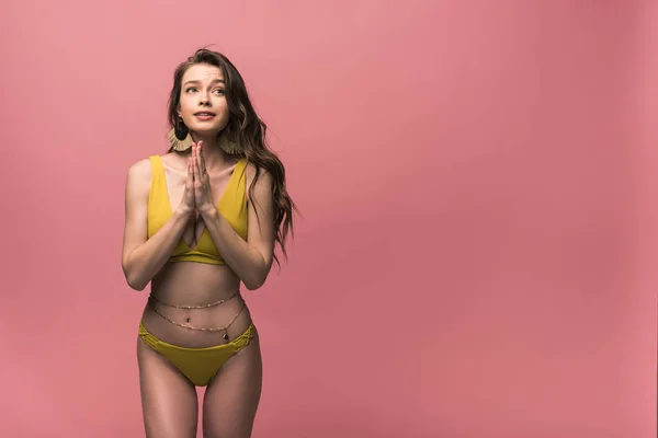 Mujer joven emocional en traje de baño amarillo que muestra por favor gesto aislado en rosa - foto de stock