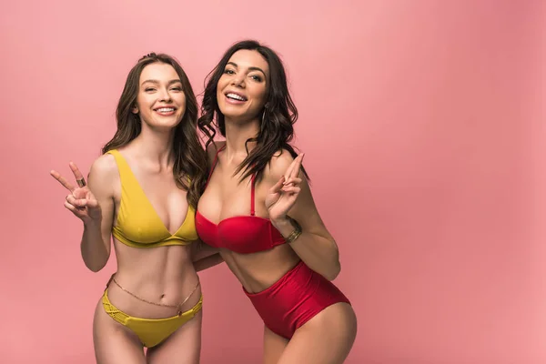 Dos chicas guapas en bikini mostrando signos de paz aisladas en rosa — Stock Photo