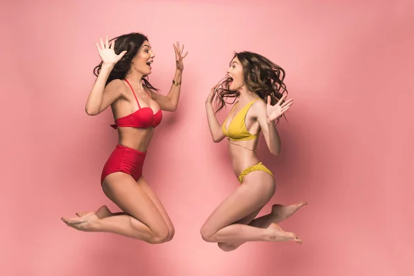 Zwei aufgeregte Mädchen im Bikini springen und schauen einander auf rosa an — Stockfoto