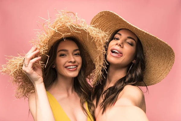 Two smiling girls in straw hats taking selfie isolated on pink — Stock Photo