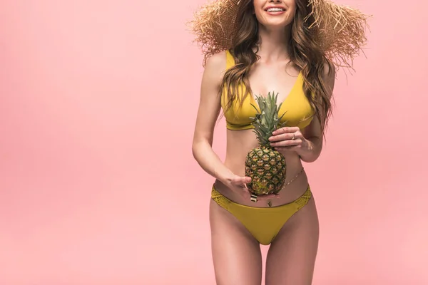 Cropped view of smiling girl in straw hat holding pineapple isolated on pink — Stock Photo