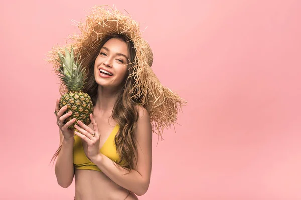Lächeln Mädchen mit Strohhut hält Ananas isoliert auf rosa — Stockfoto