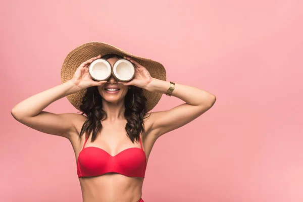 Smiling woman in straw hat and swimsuit holding coconuts isolated on pink — Stock Photo