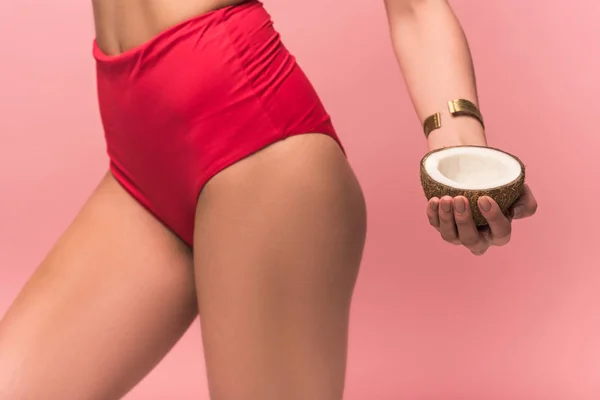 Vista recortada de la mujer en bragas sosteniendo coco cortado aislado en rosa - foto de stock