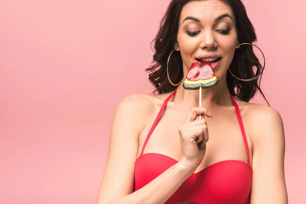 Attractive young woman in swimsuit eating watermelon lollipop isolated on pink — Stock Photo