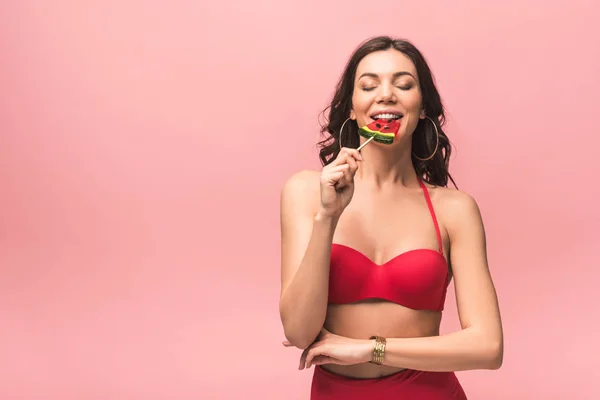 Attrayant jeune femme en maillot de bain manger pastèque sucette isolé sur rose — Photo de stock