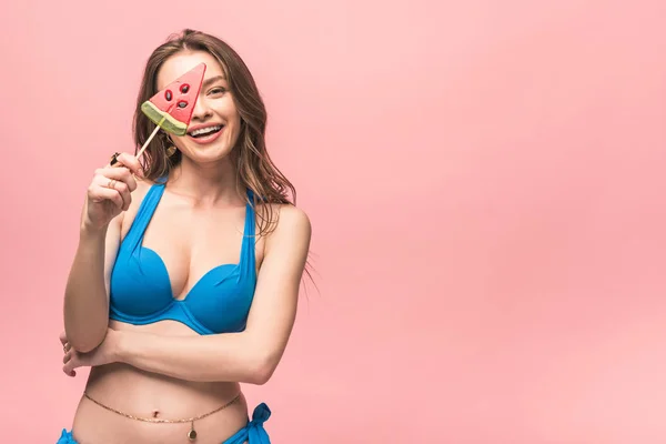 Attractive young woman in swimsuit holding watermelon lollipop isolated on pink — Stock Photo