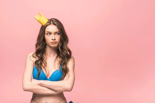 Unzufriedenes Mädchen im Bikini und Krone posiert mit verschränkten Armen auf rosa — Stockfoto