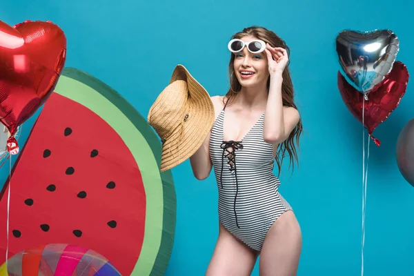 Fröhliche junge Frau mit Sonnenbrille und Strohhut auf blauem Grund — Stockfoto
